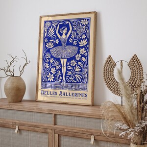 May include: A gold framed poster with a blue illustration of a ballerina dancing in a field of flowers. The text "BELLES BALLERINES" is at the bottom of the poster.
