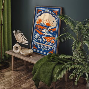 May include: A framed art print featuring a California landscape design in shades of blue, orange, and cream. The artwork depicts a sunset over mountains, palm trees, and poppies, with the word "CALIFORNIA" at the bottom. The print is displayed on a wooden bench.
