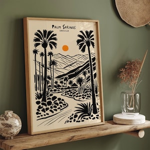 Pode incluir: Ilustra&ccedil;&atilde;o em preto e branco de palmeiras e montanhas com um sol poente ao fundo. O texto "Palm Springs, CAHUILLA" est&aacute; no topo da imagem.