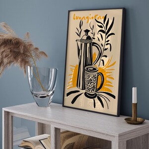 Pu&ograve; includere: Un'illustrazione in bianco e nero di una caffettiera e una tazza con il testo "Buongiorno" in una cornice nera. Lo sfondo &egrave; di colore crema con accenti gialli.