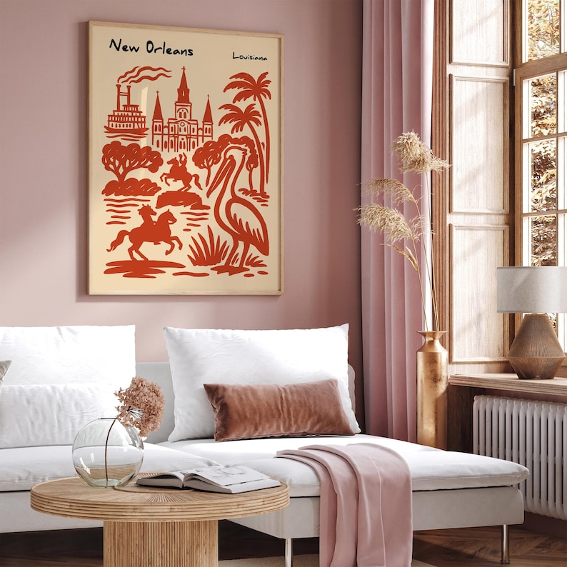 Op de afbeelding: Een ingelijste kunstprint met een gestileerde illustratie van bezienswaardigheden in New Orleans in rood op een cr&egrave;mekleurige achtergrond. De print bevat de tekst "New Orleans Louisiana". De afbeelding toont een raderstoomboot, kathedraal, palmbomen en een pelikaan.