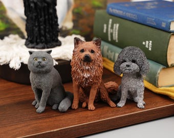 Könnte beinhalten: Drei Figuren eines Katers, eines Hundes und eines Hundes. Die Katze ist grau und hat gelbe Augen. Der erste Hund ist braun und hat ein flauschiges Fell. Der zweite Hund ist grau und hat ein flauschiges Fell. Die Figuren sitzen auf einer Holzoberfläche.