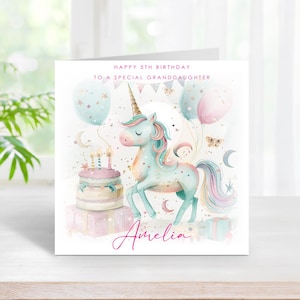 May include: A birthday card with a watercolour illustration of a unicorn, balloons, and a cake. The card reads "Happy 5th Birthday to a Special Granddaughter" and includes the name "Amelia". The design features pastel colours.