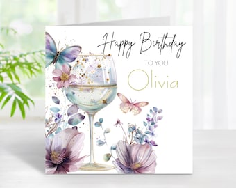 May include: A birthday card with a watercolor design. The card features a wine glass, butterflies, and floral elements in shades of purple, pink, and blue. The text reads "Happy Birthday to you Olivia."