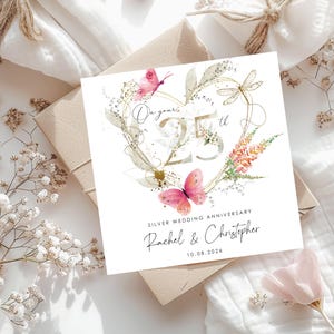 Puede incluir: Una tarjeta de felicitaci&oacute;n cuadrada con un contorno de coraz&oacute;n dorado, mariposas rosas y una lib&eacute;lula. El texto dice On your 25th, SILVER WEDDING ANNIVERSARY, Rachel & Christopher y 10.08.2026. El dise&ntilde;o incluye detalles florales en acuarela.