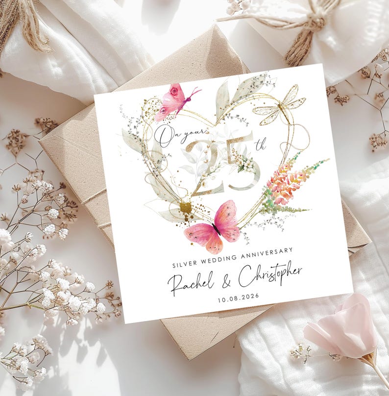 Puede incluir: Una tarjeta de felicitaci&oacute;n cuadrada con un contorno de coraz&oacute;n dorado, mariposas rosas y una lib&eacute;lula. El texto dice On your 25th, SILVER WEDDING ANNIVERSARY, Rachel & Christopher y 10.08.2026. El dise&ntilde;o incluye detalles florales en acuarela.