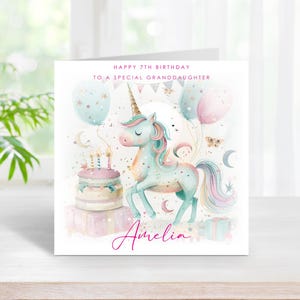 May include: A birthday card with a watercolour illustration of a unicorn, balloons, and a cake. The card reads "Happy 7th Birthday To A Special Granddaughter" and features the name "Amelia" in cursive script. Pastel colours dominate the design.