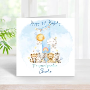 May include: A square greeting card featuring a large blue number one with a watercolour effect. The design includes a smiling sun, a cloud, stars, and a rainbow. Four illustrated animals, a tiger, elephant, lion, and zebra, sit at the base. Text reads: Happy 1st Birthday, To a special grandson, Charlie.