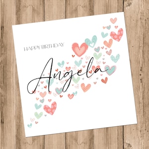 May include: A white card with the text "Happy Birthday Angela" in black script. The card is decorated with a scattering of pink, red, and blue hearts.