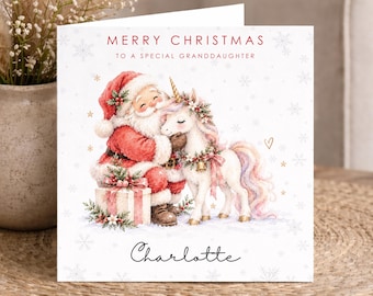 Peut inclure: Une carte de vœux de Noël carrée illustrant le Père Noël serrant dans ses bras une licorne blanche à la crinière pastel. Le texte indique MERRY CHRISTMAS TO A SPECIAL GRANDDAUGHTER et le prénom Charlotte en écriture noire en bas.