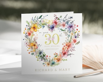 Può includere: Un biglietto bianco con un design a cuore floreale ad acquerello. Il cuore è fatto di fiori colorati e verde. Il testo sul biglietto recita "on your 30th Pearl Wedding Anniversary Richard & Mary".