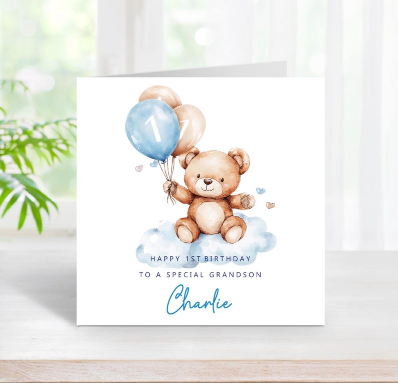 May include: A square greeting card featuring a watercolor illustration of a brown teddy bear sitting on a blue cloud, holding two balloons, one blue with the number 1 and one beige. Text reads: HAPPY 1ST BIRTHDAY TO A SPECIAL GRANDSON Charlie.