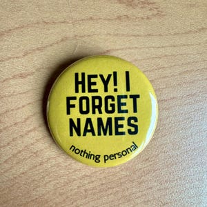 May include: Yellow button with black text that reads "HEY! I FORGET NAMES nothing personal".