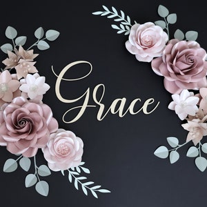 May include: A black background with a paper flower arrangement in shades of pink and white. The flowers are arranged in a semi-circle with the word "Grace" written in cursive in the center.