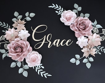 May include: A paper flower arrangement with the word "Grace" in the center. The flowers are in shades of pink and white, with green leaves. The background is black.