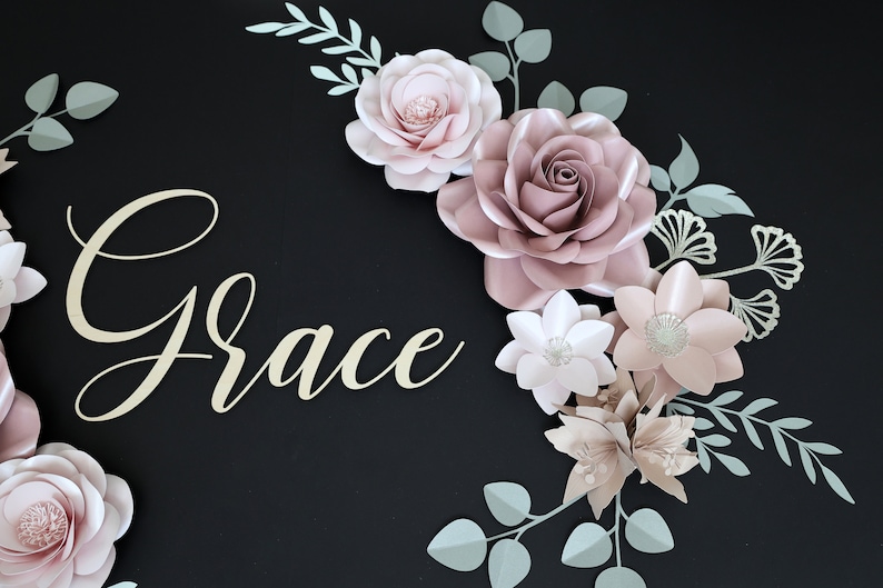 May include: A paper flower arrangement with the name "Grace" in gold script lettering. The flowers are in shades of pink and white, with green leaves.