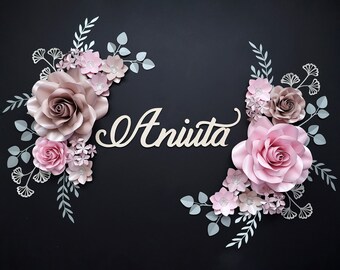 May include: A black background with a paper flower arrangement in shades of pink and brown. The flowers are arranged in two clusters, one on each side of the name "Aniita" written in cursive.