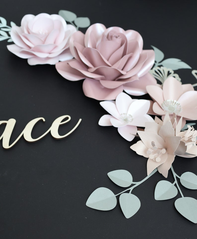 May include: A paper flower arrangement with pink and white flowers and green leaves. The word "Grace" is written in gold lettering on a black background.