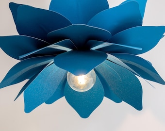 May include: A pendant light fixture shaped like a large, blooming flower with multiple layered petals in a vibrant matte blue finish. A single round, clear glass light bulb is positioned in the center, emitting a warm glow from within the petals.
