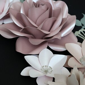 May include: A collection of paper flowers in shades of pink and white. The flowers are arranged in a cluster and have a delicate, layered appearance. The flowers are accented with silver glitter.