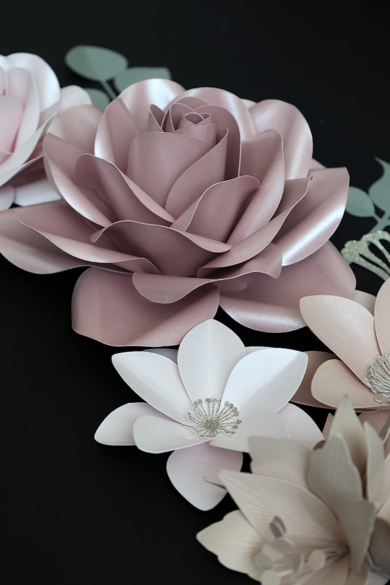 May include: A collection of paper flowers in shades of pink and white. The flowers are arranged in a cluster and have a delicate, layered appearance. The flowers are accented with silver glitter.