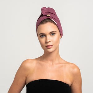 Könnte beinhalten: Ein mauvefarbenes Haartuch mit einem Holzknopf. Das Tuch ist um den Kopf einer Person gewickelt.