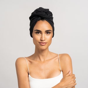 Könnte beinhalten: Eine Frau mit dunklen Haaren, die in ein schwarzes Haartuch gewickelt sind, trägt ein weißes Tanktop.