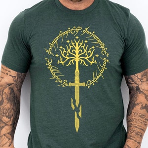 Może przedstawiać: Zielony t-shirt z nadrukiem w kolorze złotym przedstawiającym drzewo i miecz. Drzewo jest otoczone złotym okręgiem z tekstem.