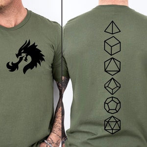 Può includere: Una maglietta verde con una grafica di un drago nero sul davanti e una fila verticale di simboli di dadi neri sul retro.