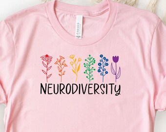 May include: A light pink t-shirt featuring a colorful floral design above the word "NEURODIVERSITY" in black. The flowers are in shades of red, orange, yellow, green, blue, and purple. The shirt is made of a soft material.