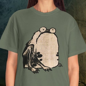 Puede incluir: Una camiseta verde con una ilustraci&oacute;n en blanco y negro de una rana en la parte delantera.