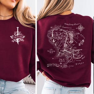 May include: Burgundy sweatshirt with a white graphic on the front that says "I AM NO MAN" with a sword and floral design. The back features a detailed map with text including "Dorchery Wasce" and "Bay of Belfalas".
