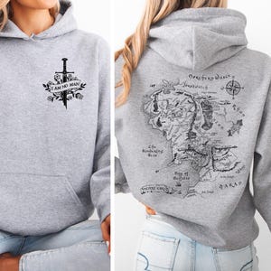 May include: A light gray hoodie with a front graphic of a sword, flowers, and the text "I AM NO MAN." The back of the hoodie features a detailed map with text and a compass rose. The hoodie has a hood and a front pocket.