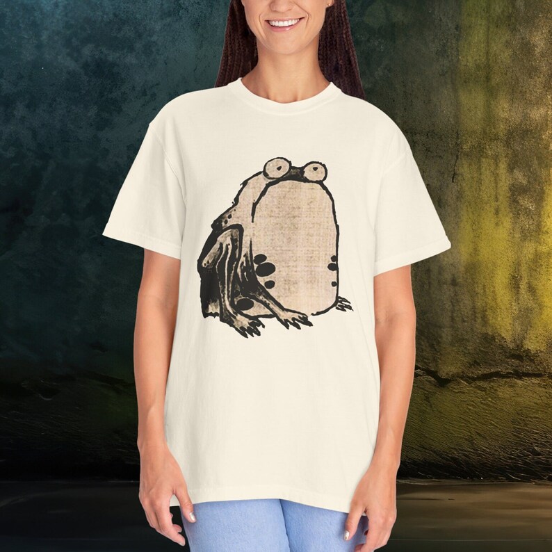 Puede incluir: Una camiseta blanca con una ilustraci&oacute;n en blanco y negro de una rana en la parte delantera.