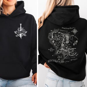 May include: Black hoodie with a white graphic on the front featuring a sword, floral elements, and the text "I AM NO MAN". The back of the hoodie displays a detailed map with text and a compass rose.