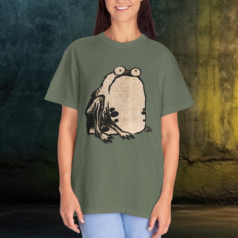 Puede incluir: Una camiseta verde con una ilustraci&oacute;n en blanco y negro de una rana en la parte delantera.