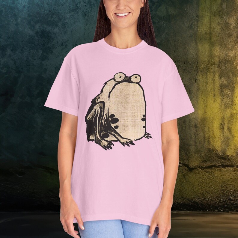 Puede incluir: Una camiseta rosa con una ilustraci&oacute;n en blanco y negro de una rana en la parte delantera.