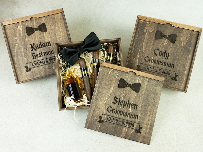 May include: Three wooden gift boxes with personalized engravings for a best man and groomsmen. Each box includes a bow tie, miniature liquor bottle, and cigars.