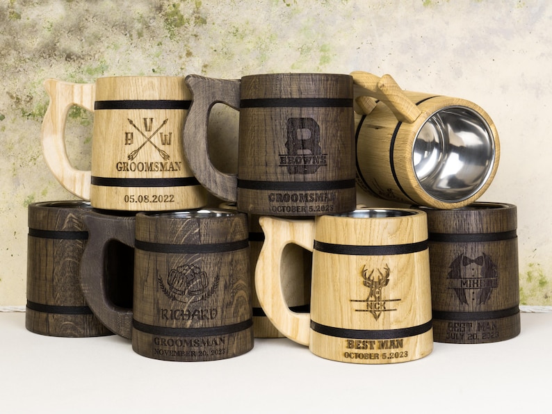 May include: A selection of wooden beer tankards with stainless steel interiors. The tankards are engraved with names, dates, and titles such as "Groomsman" and "Best Man." The mugs have a rustic, handcrafted appearance.