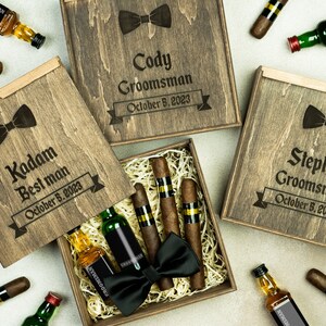 May include: Three wooden gift boxes with engraved text, each containing a miniature bottle of liquor, cigars, and a bow tie. The boxes are labeled "Kadam Best Man October 5, 2023", "Cody Groomsman October 5, 2023", and "Stephen Groomsman October 5, 2023".