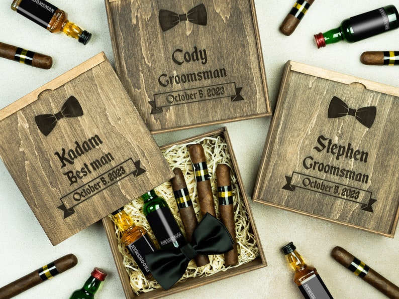 May include: Three wooden gift boxes with engraved text, each containing a miniature bottle of liquor, cigars, and a bow tie. The boxes are labeled "Kadam Best Man October 5, 2023", "Cody Groomsman October 5, 2023", and "Stephen Groomsman October 5, 2023".
