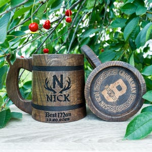 May include: Two wooden beer tankards with engraved details. One tankard features the name "Nick" with an initial and antlers, and the text "Best Man 10.20.2025." The other tankard's lid says "Groomsman Browns 10.20.2025."