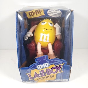以下が含まれることがあります： 透明なプラスチックの箱に入った、黄色のM&M'sキャンディディスペンサー。 ディスペンサーは、赤いLa-Z-Boyチェアに座っているM&M'sのキャラクターの形をしています。 箱には「M&M's LA-Z-BOY DISPENSER」と「キャンディ5.60オンス入り」と書かれています。