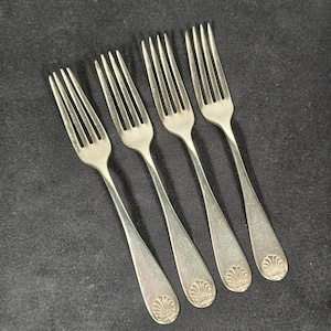 Peut inclure: Quatre fourchettes argentées avec un motif de coquillage sur le manche. Les fourchettes sont disposées en diagonale sur un fond sombre, mettant en valeur leurs dents et leurs manches allongés. La coutellerie semble être vintage.