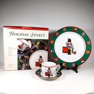 May include: A 12-piece Holiday Spirit dinnerware set featuring a festive nutcracker design. The set includes dinner plates, cups, and saucers. The plates have a green border with drum illustrations. The box reads "Holiday Spirit".