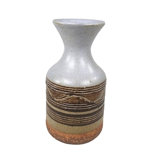 May include: A ceramic vase with a light grey upper section and a brown and tan striped lower section. The vase has a narrow neck and a wider base, with a textured, handcrafted appearance. The vase is approximately 20 cm tall.