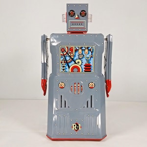 Pode incluir: Um brinquedo robô de metal cinza com detalhes vermelhos e uma ilustração detalhada de engrenagens e luzes no peito. O robô tem uma cabeça redonda com olhos vermelhos e uma boca preta. O robô está etiquetado como "R-1" no peito.