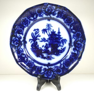 Puede incluir: Un plato de porcelana azul y blanco con un borde decorativo y una imagen central de una pagoda y árboles. El plato es octogonal y tiene un acabado brillante.