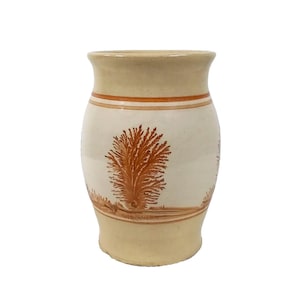 May include: A cream-coloured ceramic vase with a brown tree design. The vase has a rounded body and a slightly flared lip.