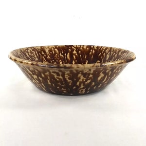 May include: A brown and cream speckled ceramic bowl. The bowl is round and has a slight lip around the edge.